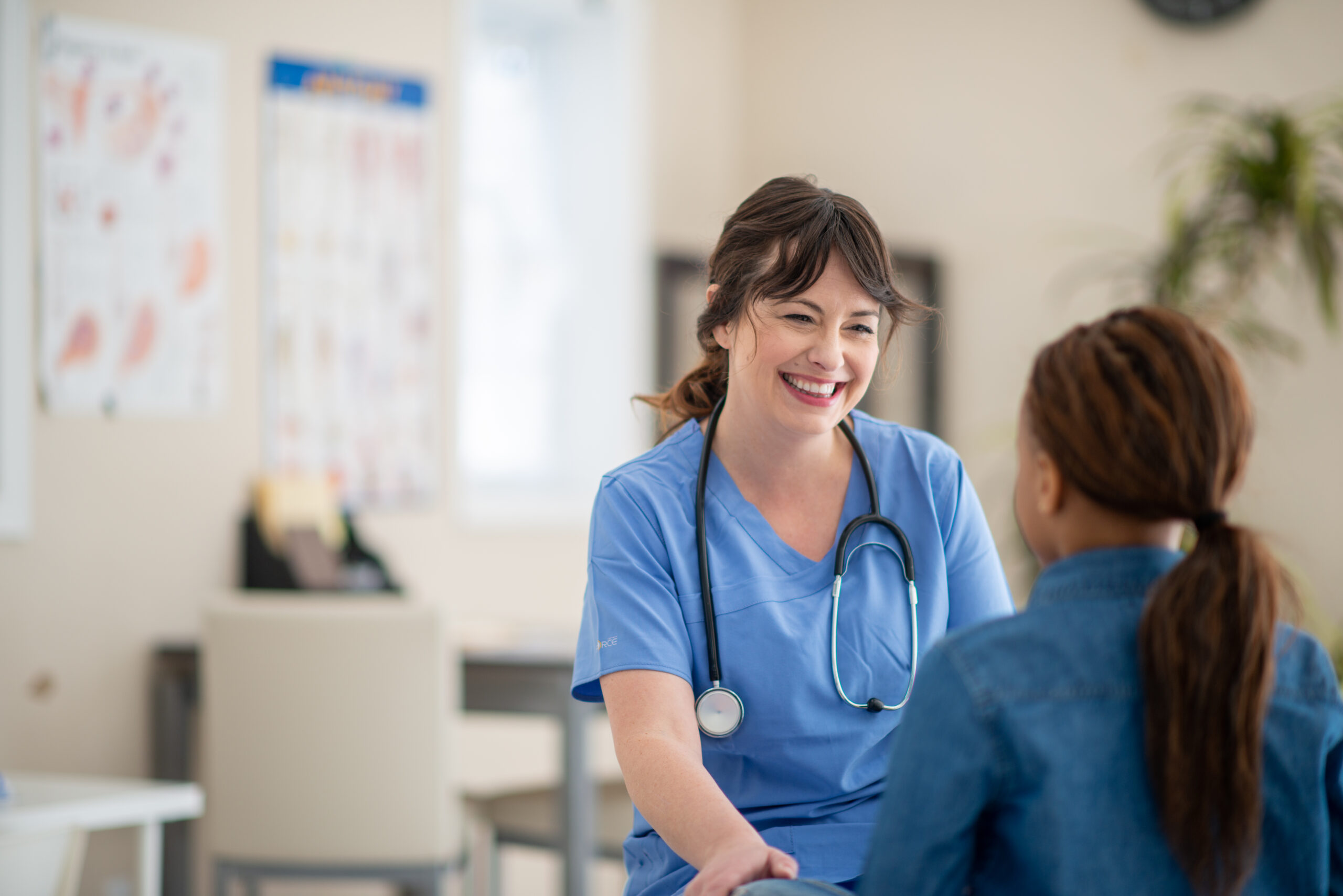 Woman wearing scrubs and a stethoscope talking to a patient.