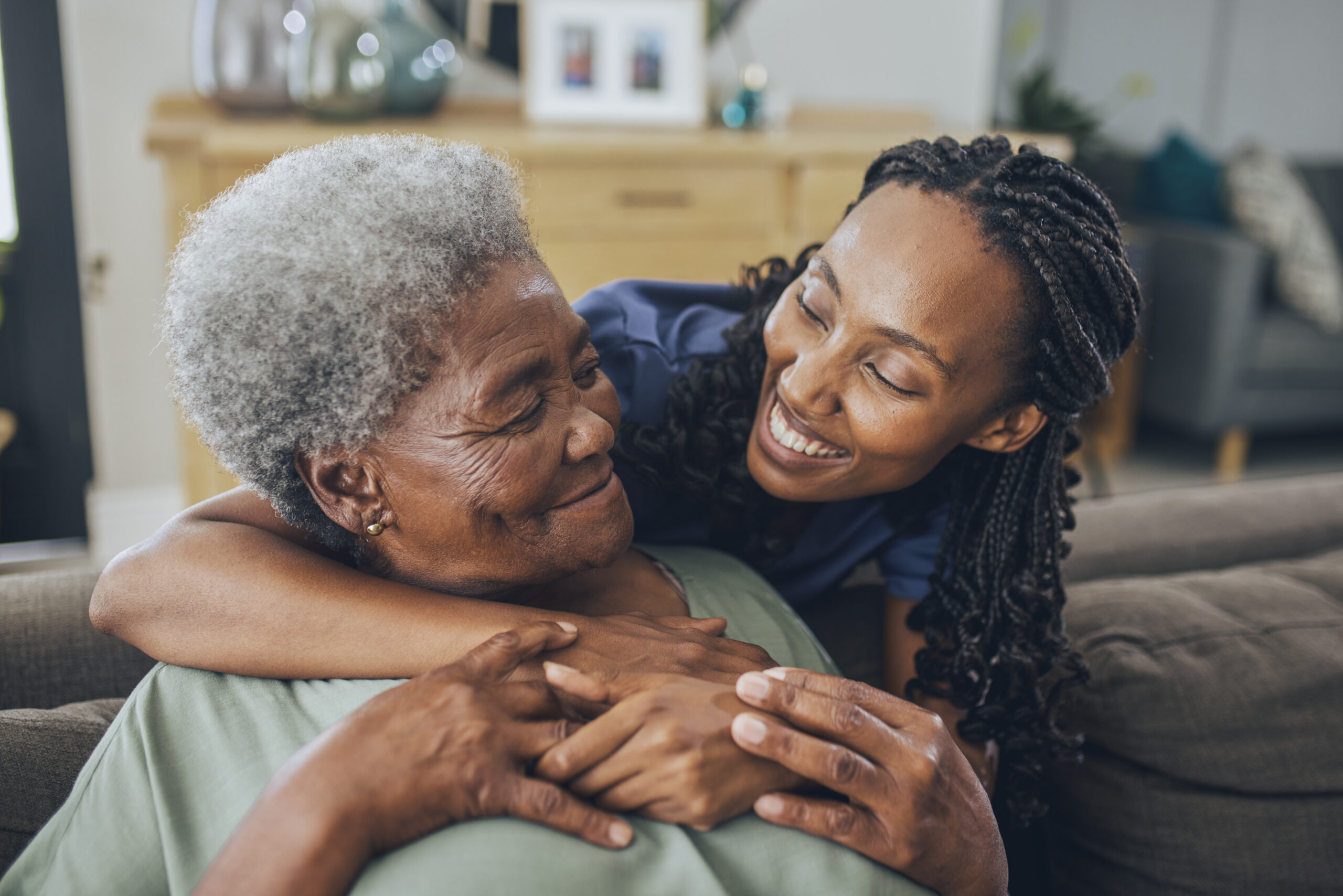 A nurse bending down and hugging an old woman who is sitting down.