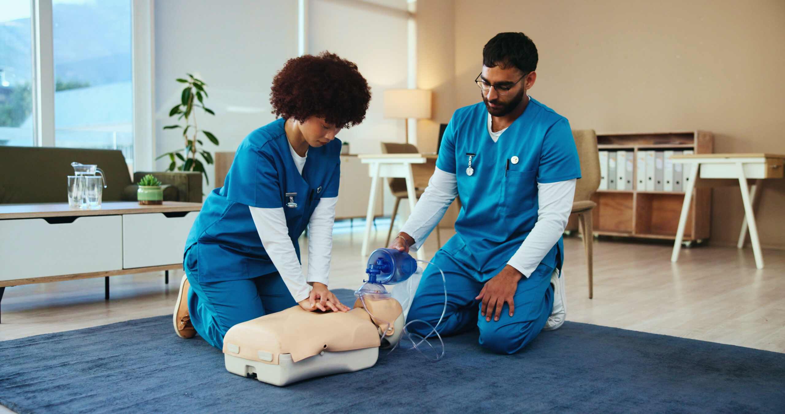 Two nursing students in scrubs practicing CPR on a dummy.