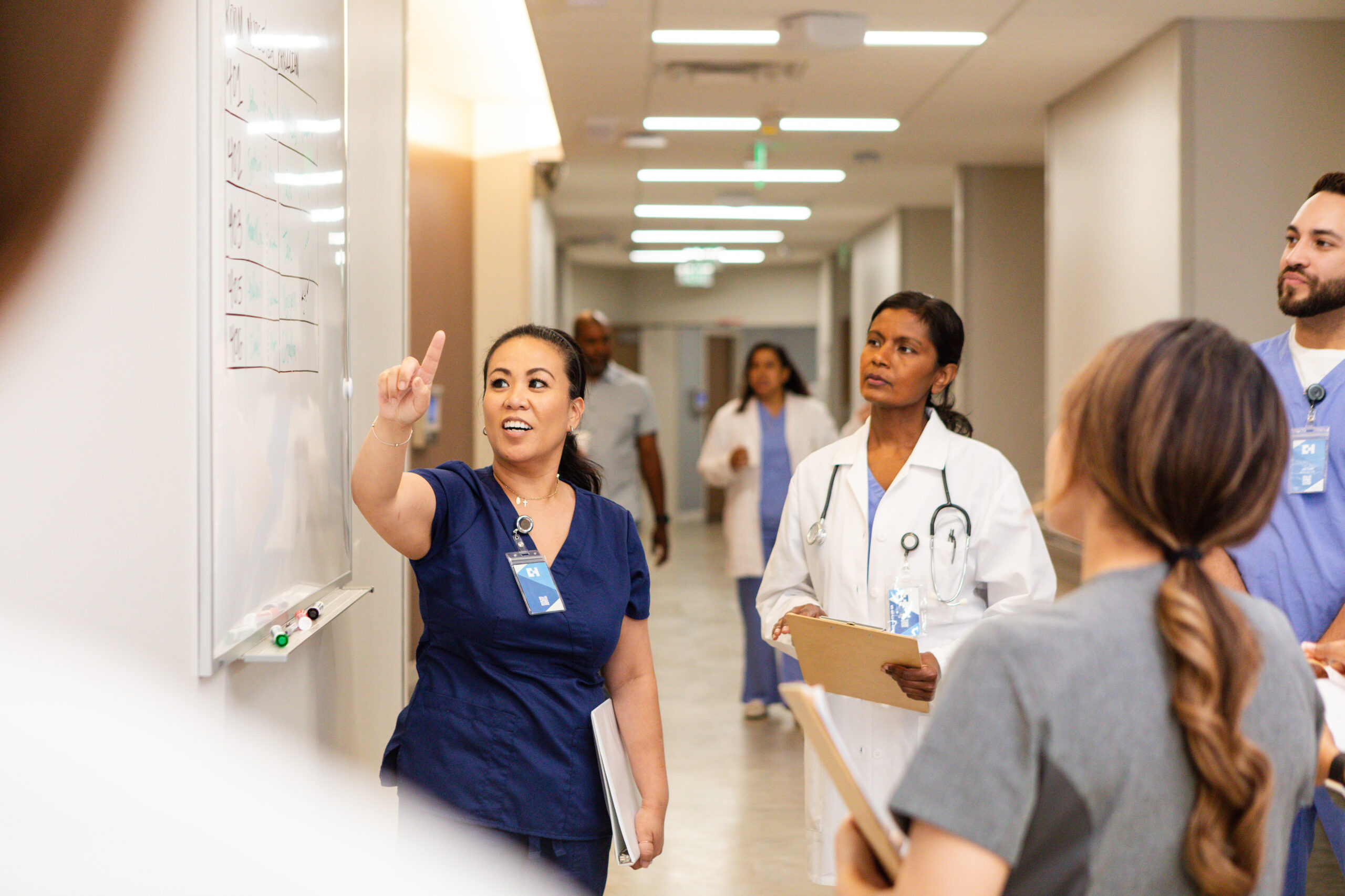 Woman in scrubs pointing to a whiteboard with nursing students around her.