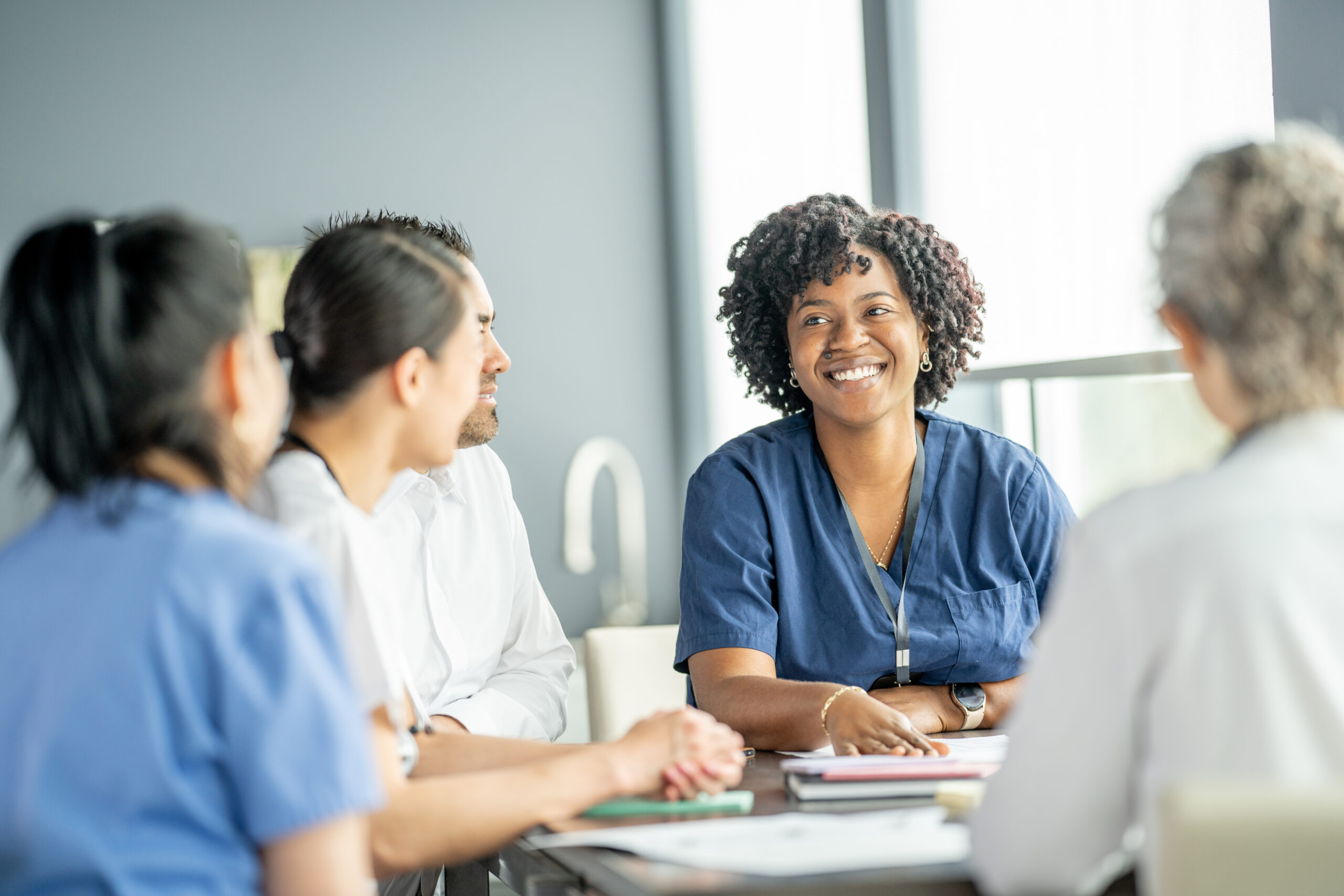 Woman sitting at a table with other women wearing scrubs.